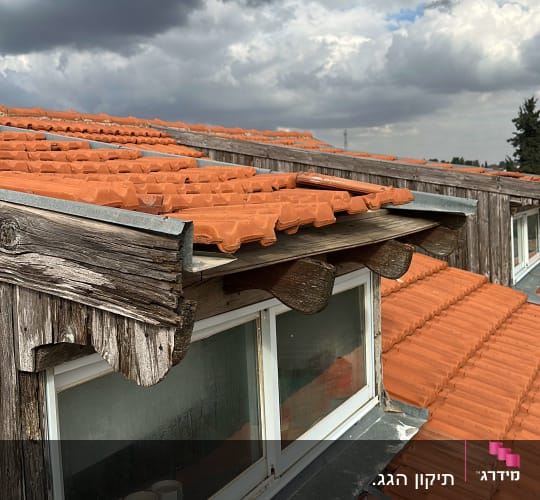 גג רעפים עם חלון עץ תחת שמיים מעוננים